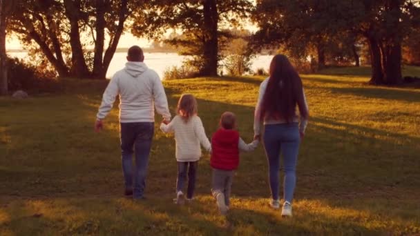 Amar los paseos familiares en el campo durante el atardecer. Mamá y papá abrazan y juegan con su hijo y su hija. El concepto de amor, cuidado parental e hijos. — Vídeos de Stock