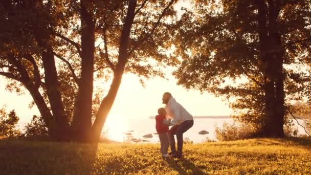 Liebevolle Familienspaziergänge in der Natur während des Sonnenuntergangs. Papa spielt mit seinem Sohn. Das Konzept der Liebe, der elterlichen Sorge und der Kinder. — Stockvideo