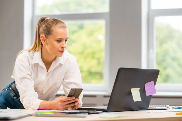 Рабочее место фрилансера или студентки в домашнем офисе. Молодая женщина работает на компьютере и других устройствах. Дистанционная концепция работы. — стоковое фото