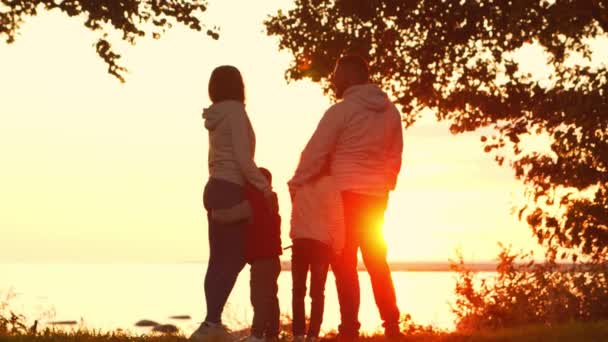 Milující rodinné procházky po venkově během západu slunce. Máma s tátou se objímají a hrají si se synem a dcerou. Koncept lásky, rodičovské péče a dětí. — Stock video