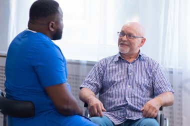Bakıcı ve tekerlekli sandalyedeki yaşlı adam. Bakımevindeki profesyonel hemşire ve hasta. Yardım, rehabilitasyon ve sağlık hizmetleri.