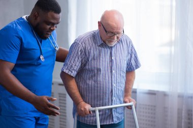 Bakıcı yaşlı adama Walker 'la yürümeyi öğretiyor. Bakımevindeki profesyonel hemşire ve hasta. Yardım, rehabilitasyon ve sağlık.