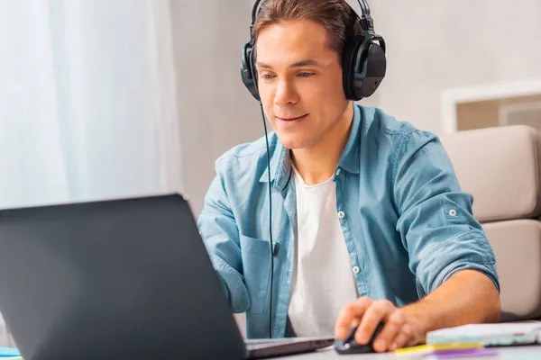 Młody człowiek w słuchawkach pracuje na laptopie w domu. Koncepcja pracy zdalnej i kształcenia. — Zdjęcie stockowe