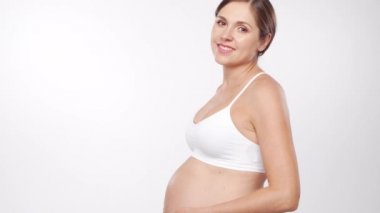 Genç, mutlu ve sağlıklı hamile bir kadın beyaz arka planda. Stüdyo videosu. Bebek beklentisi, hamilelik ve annelik kavramı.