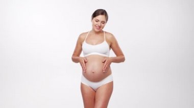 Genç, mutlu ve sağlıklı hamile bir kadın beyaz arka planda. Stüdyo videosu. Bebek beklentisi, hamilelik ve annelik kavramı.