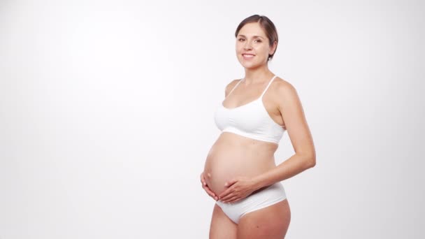 Jeune femme enceinte heureuse et en bonne santé sur fond blanc. Vidéo studio. Concept d'attente, de grossesse et de maternité du bébé. — Video