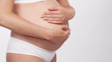 Genç, mutlu ve sağlıklı hamile bir kadın beyaz arka planda. Stüdyo videosu. Bebek beklentisi, hamilelik ve annelik kavramı.