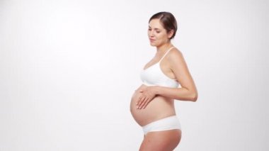 Genç, mutlu ve sağlıklı hamile bir kadın beyaz arka planda. Stüdyo videosu. Bebek beklentisi, hamilelik ve annelik kavramı.