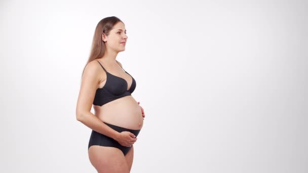젊고 행복하고 건강 한 임산부가 하얀 배경에 있어요. 스튜디오 비디오. 아기에 대한 기대, 임신 및 어머니의 개념. — 비디오