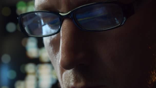 Retrato de cerca de un joven que trabaja en la computadora. La pantalla del ordenador portátil se refleja en las gafas. Luces nocturnas en el fondo. Concepto de negocio, codificación e intercambio. — Vídeos de Stock