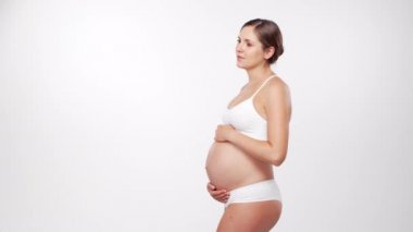 Genç, mutlu ve sağlıklı hamile bir kadın beyaz arka planda. Stüdyo videosu. Bebek beklentisi, hamilelik ve annelik kavramı.