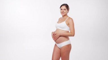 Genç, mutlu ve sağlıklı hamile bir kadın beyaz arka planda. Stüdyo videosu. Bebek beklentisi, hamilelik ve annelik kavramı.