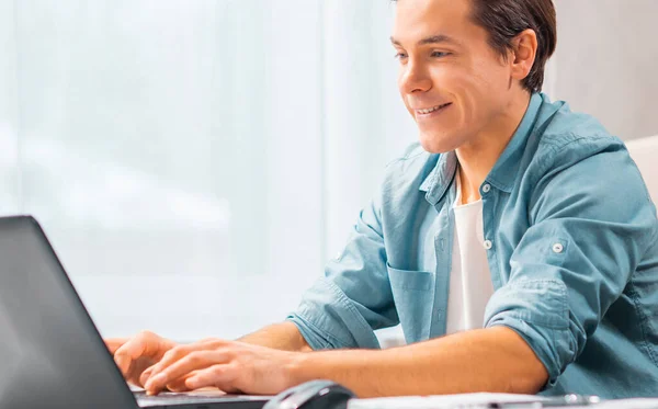 El joven trabaja en una computadora portátil. Freelancer, trabajador remoto o lugar de trabajo estudiantil. Concepto de trabajo distante. — Foto de Stock