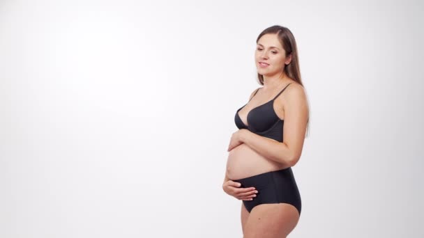 Jonge, gelukkige en gezonde zwangere vrouw op witte achtergrond. Studio video. Baby verwachting, zwangerschap en moederschap concept. — Stockvideo