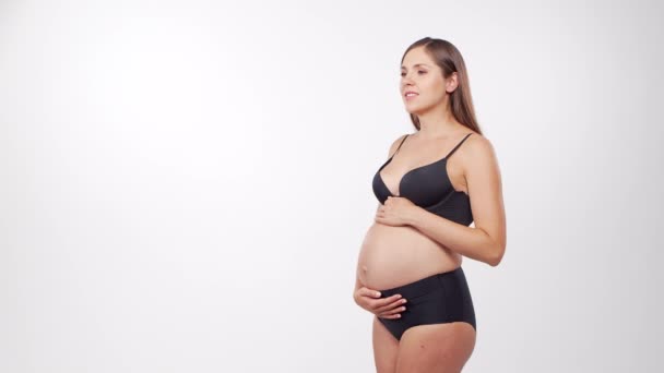 Jeune femme enceinte heureuse et en bonne santé sur fond blanc. Vidéo studio. Concept d'attente, de grossesse et de maternité du bébé. — Video