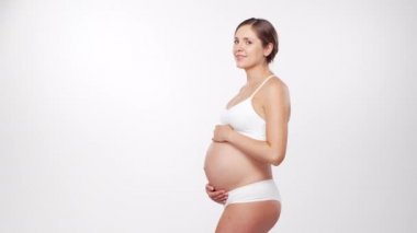 Genç, mutlu ve sağlıklı hamile bir kadın beyaz arka planda. Stüdyo videosu. Bebek beklentisi, hamilelik ve annelik kavramı.