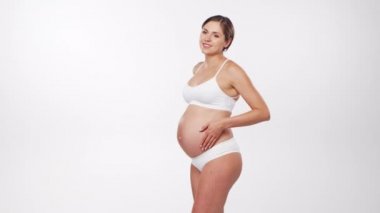 Genç, mutlu ve sağlıklı hamile bir kadın beyaz arka planda. Stüdyo videosu. Bebek beklentisi, hamilelik ve annelik kavramı.