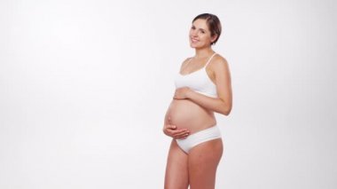 Genç, mutlu ve sağlıklı hamile bir kadın beyaz arka planda. Stüdyo videosu. Bebek beklentisi, hamilelik ve annelik kavramı.