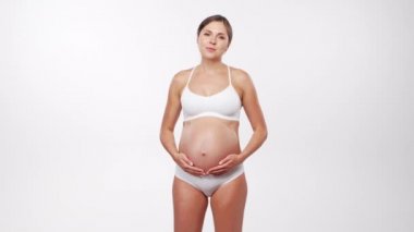 Genç, mutlu ve sağlıklı hamile bir kadın beyaz arka planda. Stüdyo videosu. Bebek beklentisi, hamilelik ve annelik kavramı.