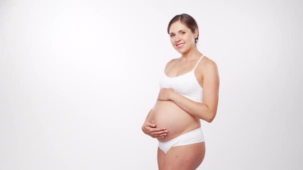 Jeune femme enceinte heureuse et en bonne santé sur fond blanc. Vidéo studio. Concept d'attente, de grossesse et de maternité du bébé. — Video