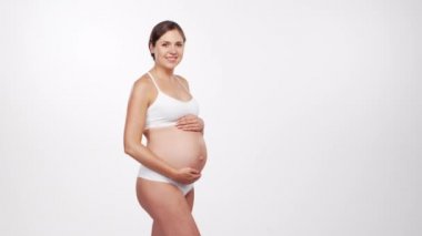 Genç, mutlu ve sağlıklı hamile bir kadın beyaz arka planda. Stüdyo videosu. Bebek beklentisi, hamilelik ve annelik kavramı.