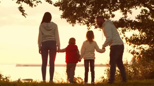 Liebevolle Familienspaziergänge in der Natur während des Sonnenuntergangs. Mama und Papa umarmen und spielen mit ihrem Sohn und ihrer Tochter. Das Konzept der Liebe, der elterlichen Sorge und der Kinder. — Stockvideo