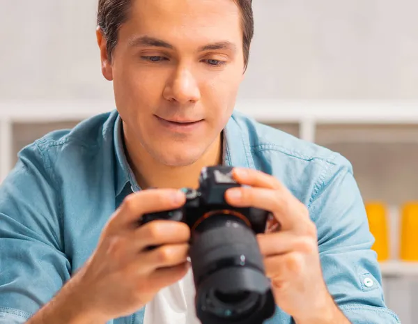 Freischaffende Fotografen am Arbeitsplatz. Ein junger Mann mit Kamera sitzt an einem Tisch und betrachtet Fotos. Fernarbeits-Konzept. — Stockfoto