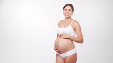 Genç, mutlu ve sağlıklı hamile bir kadın beyaz arka planda. Stüdyo videosu. Bebek beklentisi, hamilelik ve annelik kavramı.