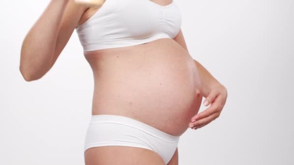หญิงสาวที่มีความสุขและมีสุขภาพดีตั้งครรภ์บนพื้นหลังสีขาว วิดีโอสตูดิโอ ความคาดหวังของทารก การตั้งครรภ์ และการเป็นแม่ . — วีดีโอสต็อก
