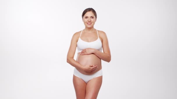 Jeune femme enceinte heureuse et en bonne santé sur fond blanc. Vidéo studio. Concept d'attente, de grossesse et de maternité du bébé. — Video