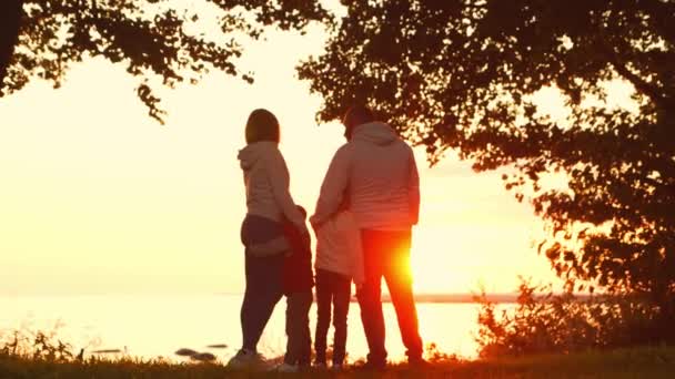 Aimant les promenades en famille dans la campagne pendant le coucher du soleil. Maman et papa s'embrassent et jouent avec leur fils et leur fille. Le concept d'amour, de soins parentaux et d'enfants. — Video