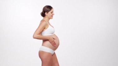 Genç, mutlu ve sağlıklı hamile bir kadın beyaz arka planda. Stüdyo videosu. Bebek beklentisi, hamilelik ve annelik kavramı.