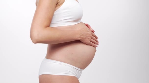 Jeune femme enceinte heureuse et en bonne santé sur fond blanc. Vidéo studio. Concept d'attente, de grossesse et de maternité du bébé. — Video