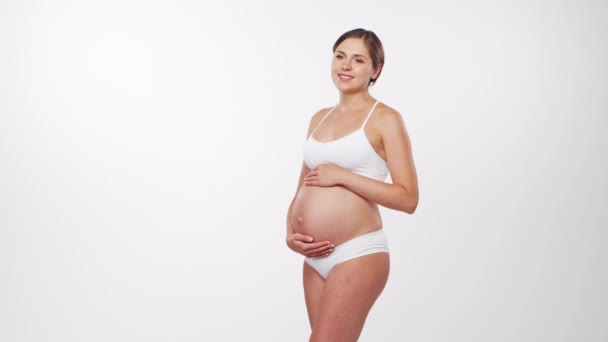 Mujer embarazada joven, feliz y saludable sobre fondo blanco. Vídeo del estudio. Esperanza del bebé, embarazo y concepto de maternidad. — Vídeo de stock