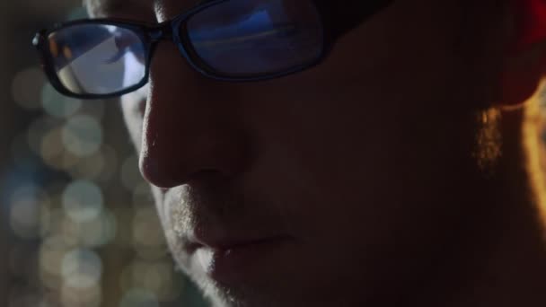 Retrato de cerca de un joven que trabaja en la computadora. La pantalla del ordenador portátil se refleja en las gafas. Luces nocturnas en el fondo. Concepto de negocio, codificación e intercambio. — Vídeos de Stock