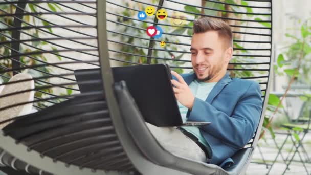 Joven influenciador o blogger observa un feed de noticias de redes sociales, obtiene likes y vistas en forma de emoji animado. El concepto de redes sociales, internet y comunicaciones en línea. — Vídeo de stock