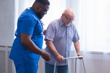 Bakıcı yaşlı adama Walker 'la yürümeyi öğretiyor. Bakımevindeki profesyonel hemşire ve hasta. Yardım, rehabilitasyon ve sağlık.