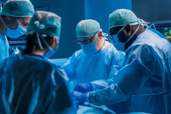 Multiracial team of professional medical surgeons performs the surgical operation in a modern hospital. Doctors are working to save the patient. Medicine, health, cardiology and transplantation. — Stock Photo, Image