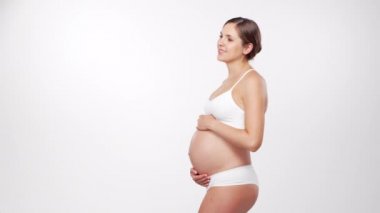 Genç, mutlu ve sağlıklı hamile bir kadın beyaz arka planda. Stüdyo videosu. Bebek beklentisi, hamilelik ve annelik kavramı.