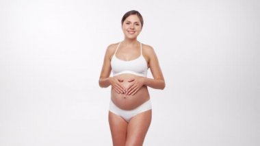 Genç, mutlu ve sağlıklı hamile bir kadın beyaz arka planda. Stüdyo videosu. Bebek beklentisi, hamilelik ve annelik kavramı.