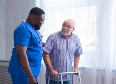 Bakıcı yaşlı adama Walker 'la yürümeyi öğretiyor. Bakımevindeki profesyonel hemşire ve hasta. Yardım, rehabilitasyon ve sağlık.
