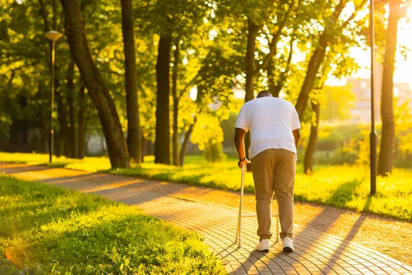 De man loopt met een wandelaar buiten bij zonsondergang. Revalidatieconcept. — Stockfoto