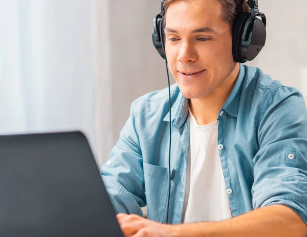 Egy fiatal férfi fejhallgatóban egy laptop számítógépen dolgozik otthon. Távmunka és oktatási koncepció. — Stock Fotó
