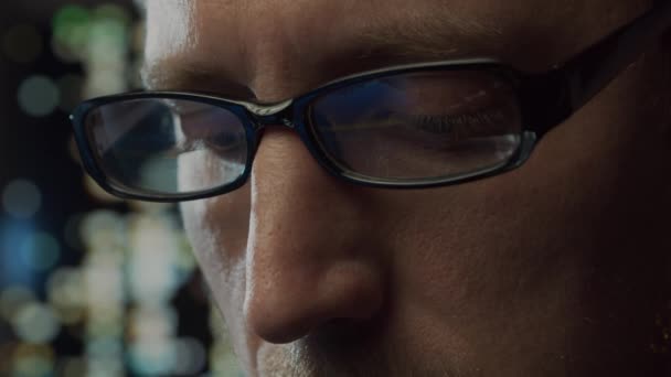 Retrato de cerca de un joven que trabaja en la computadora. La pantalla del ordenador portátil se refleja en las gafas. Luces nocturnas en el fondo. Concepto de negocio, codificación e intercambio. — Vídeo de stock