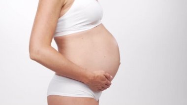 Genç, mutlu ve sağlıklı hamile bir kadın beyaz arka planda. Stüdyo videosu. Bebek beklentisi, hamilelik ve annelik kavramı.