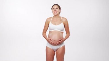 Genç, mutlu ve sağlıklı hamile bir kadın beyaz arka planda. Stüdyo videosu. Bebek beklentisi, hamilelik ve annelik kavramı.