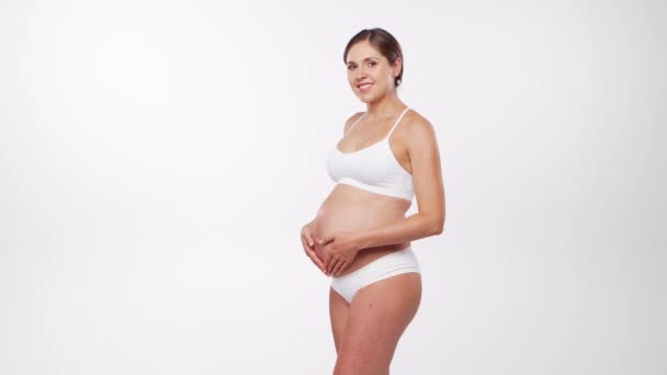 Молодая, счастливая и здоровая беременная женщина на белом фоне. Студийное видео Ожидание ребенка, беременность и материнство. — стоковое видео