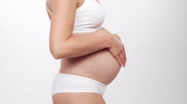 Genç, mutlu ve sağlıklı hamile bir kadın beyaz arka planda. Stüdyo videosu. Bebek beklentisi, hamilelik ve annelik kavramı.