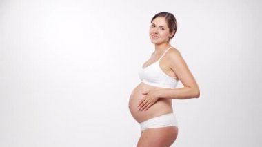 Genç, mutlu ve sağlıklı hamile bir kadın beyaz arka planda. Stüdyo videosu. Bebek beklentisi, hamilelik ve annelik kavramı.