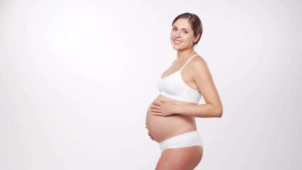 Jonge, gelukkige en gezonde zwangere vrouw op witte achtergrond. Studio video. Baby verwachting, zwangerschap en moederschap concept. — Stockvideo